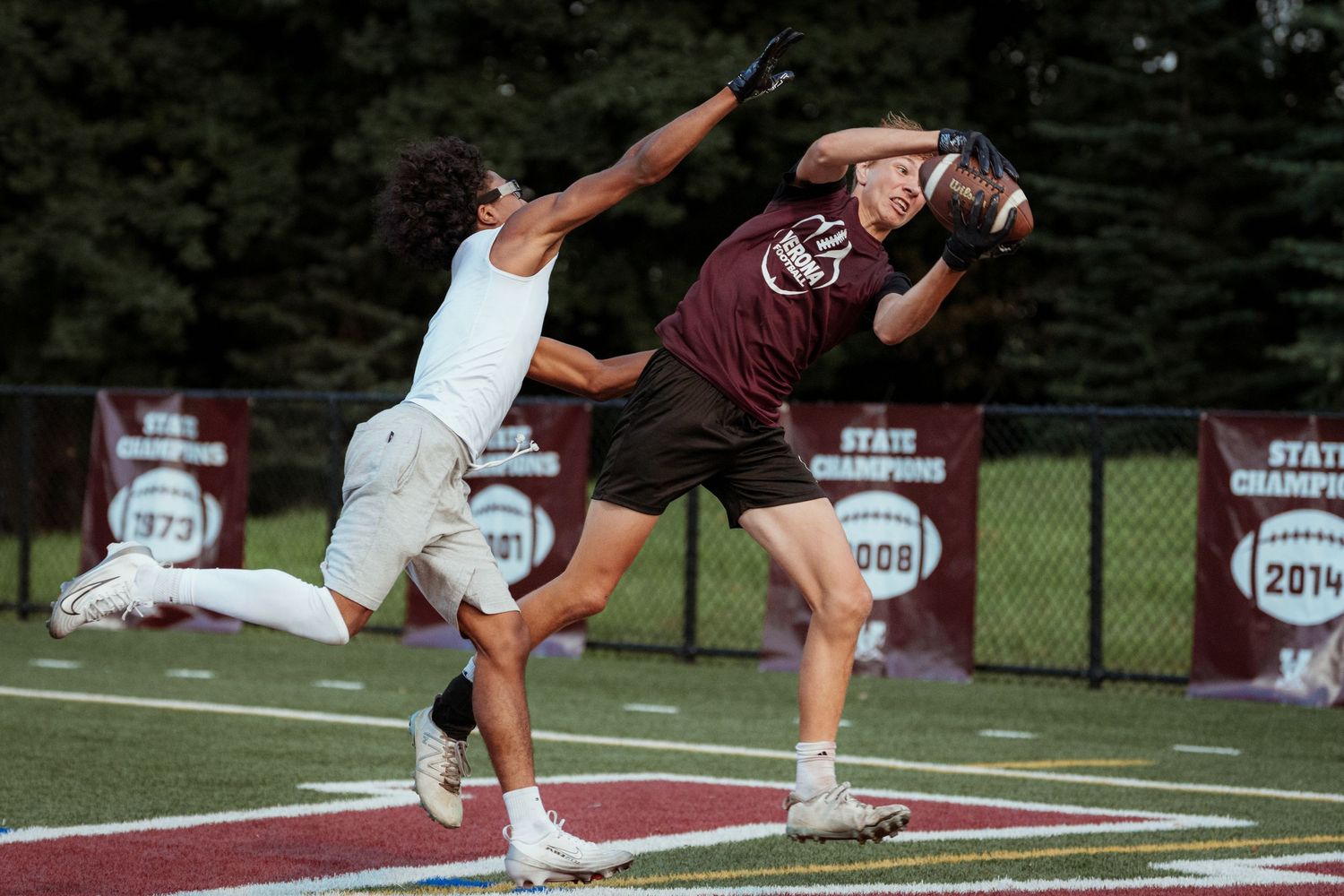 Two athletes compete for a catch during an intense football play on a turf field.