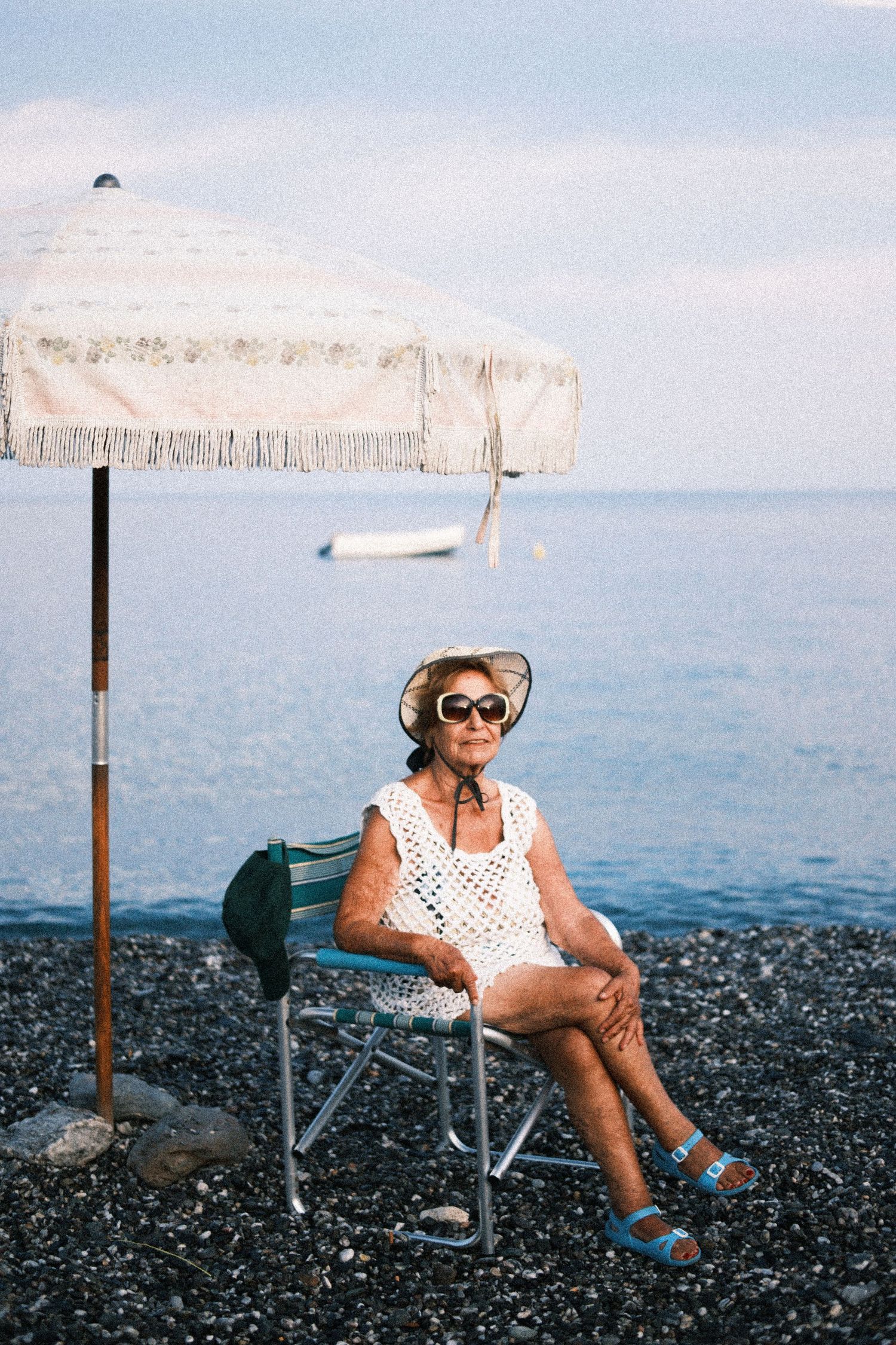 Person relaxing in a beach chair on a black pebble beach with blue ocean and white cliffs in the background.