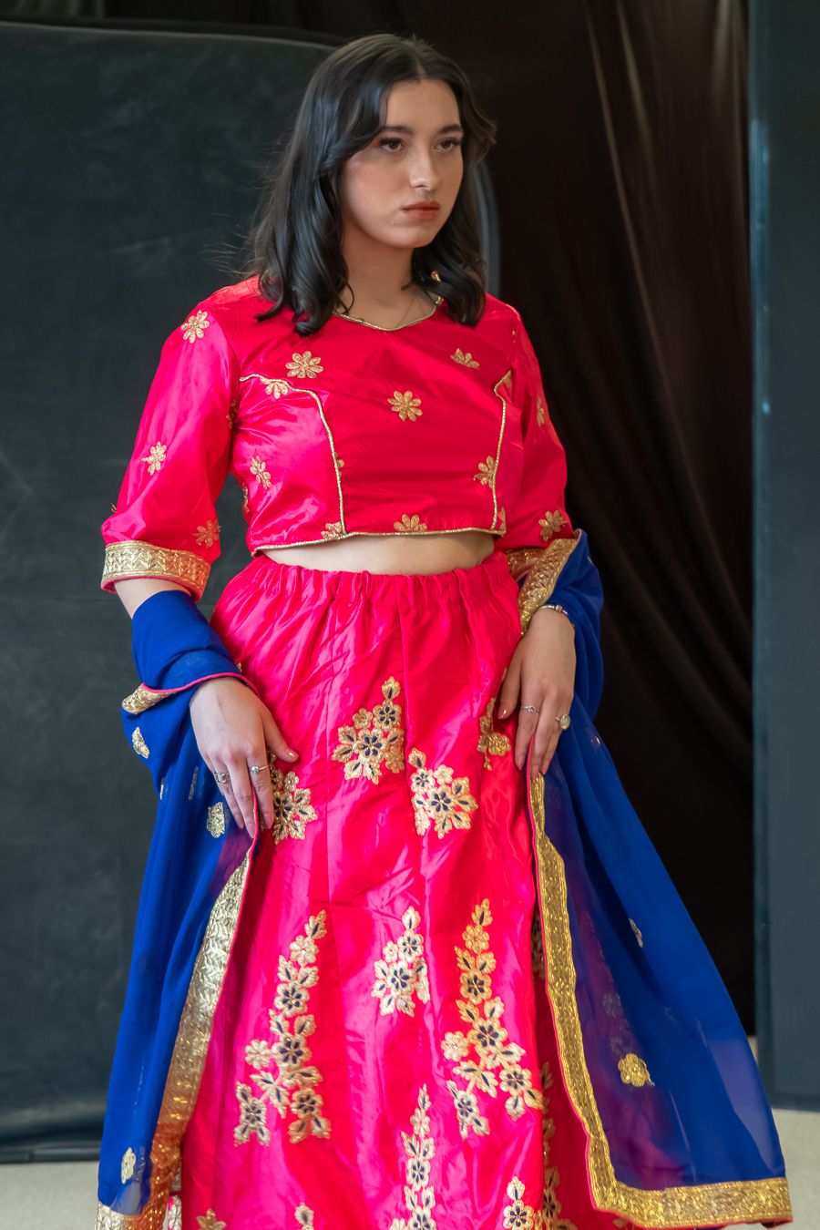 Traditional Indian attire featuring a bright pink anarkali dress with gold embroidery and royal blue dupatta.