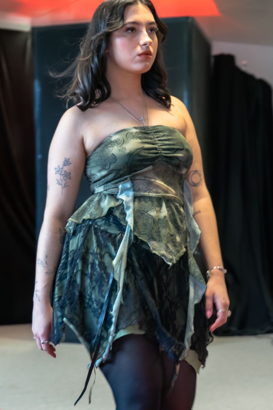 A person wearing a distressed green dress poses in different angles showing details of the unique garment design.