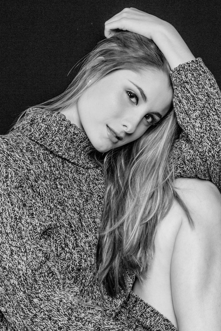 Artistic black and white fashion series with model in textured top laying against dark background.