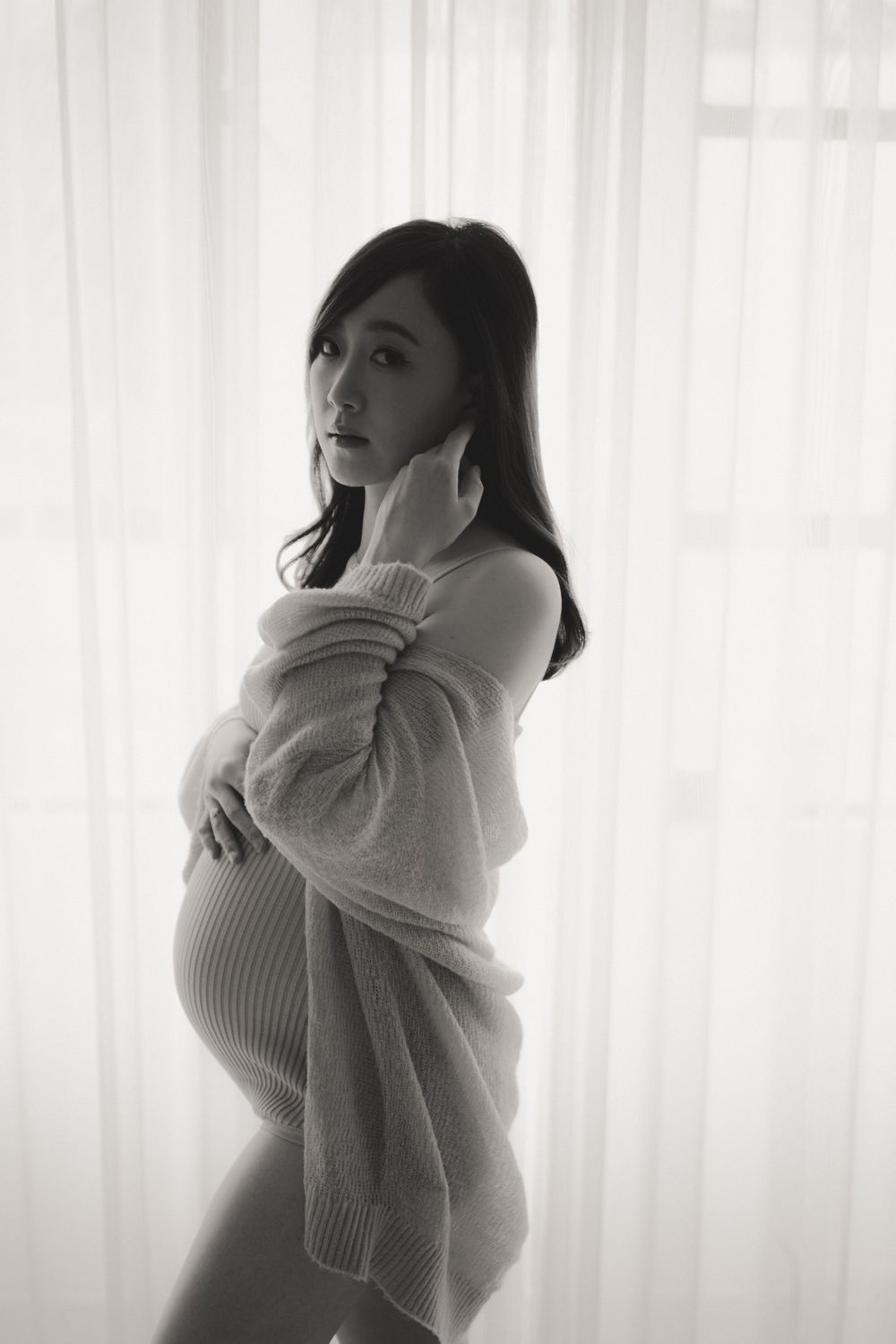 A black and white artistic portrait series showing a figure in soft lighting against sheer curtains wearing a white sweater.