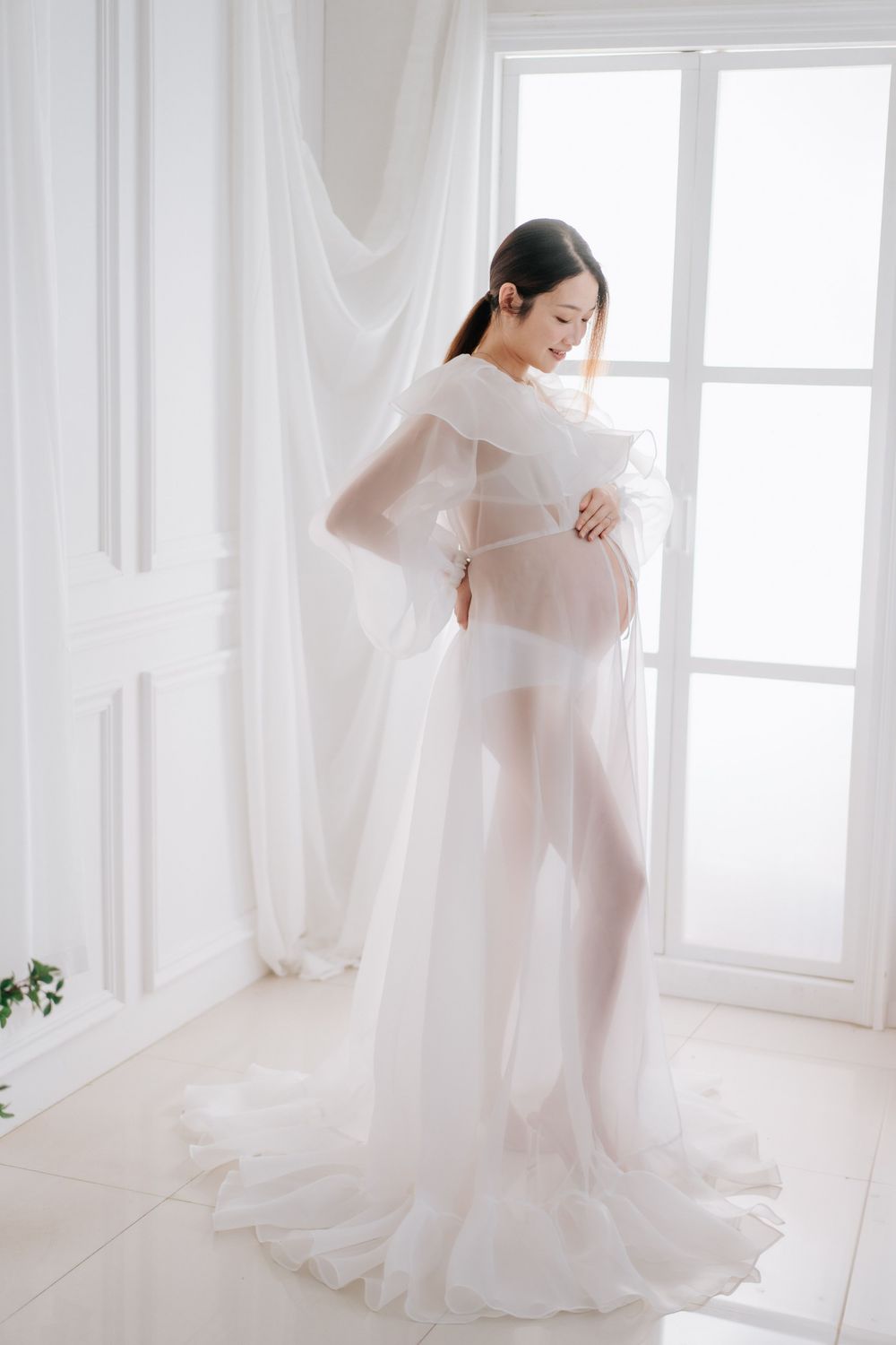 Ethereal maternity photography series showing flowing white fabric and natural window light in a bright studio setting.