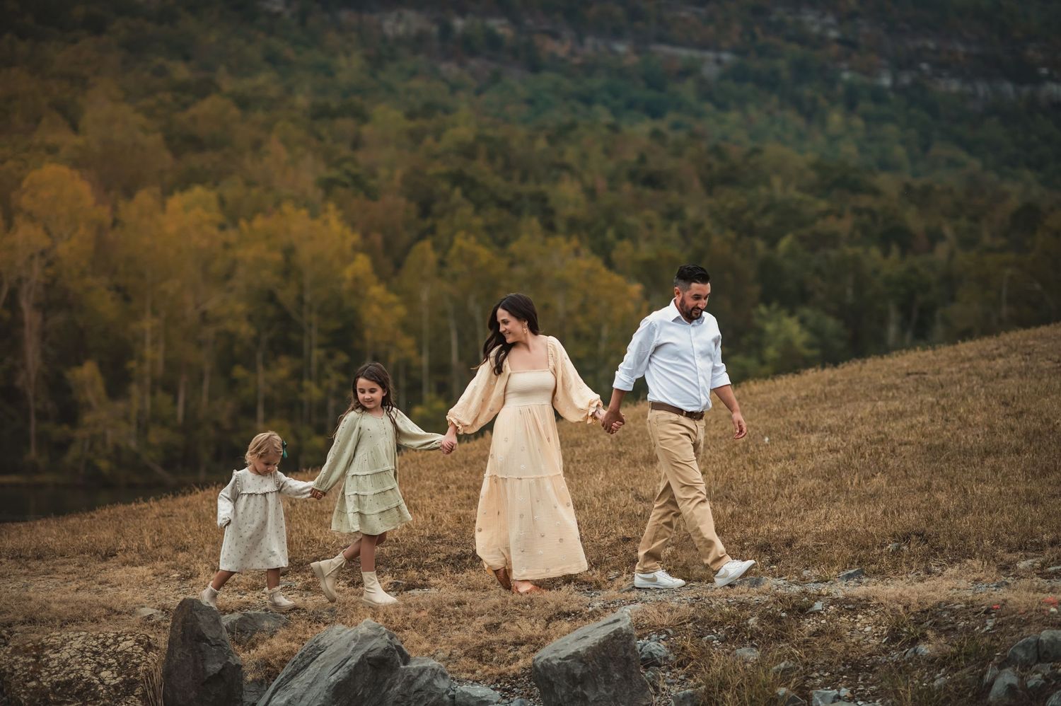 mom and dad hug young daughters from behind on the edge of a dock for family photo session