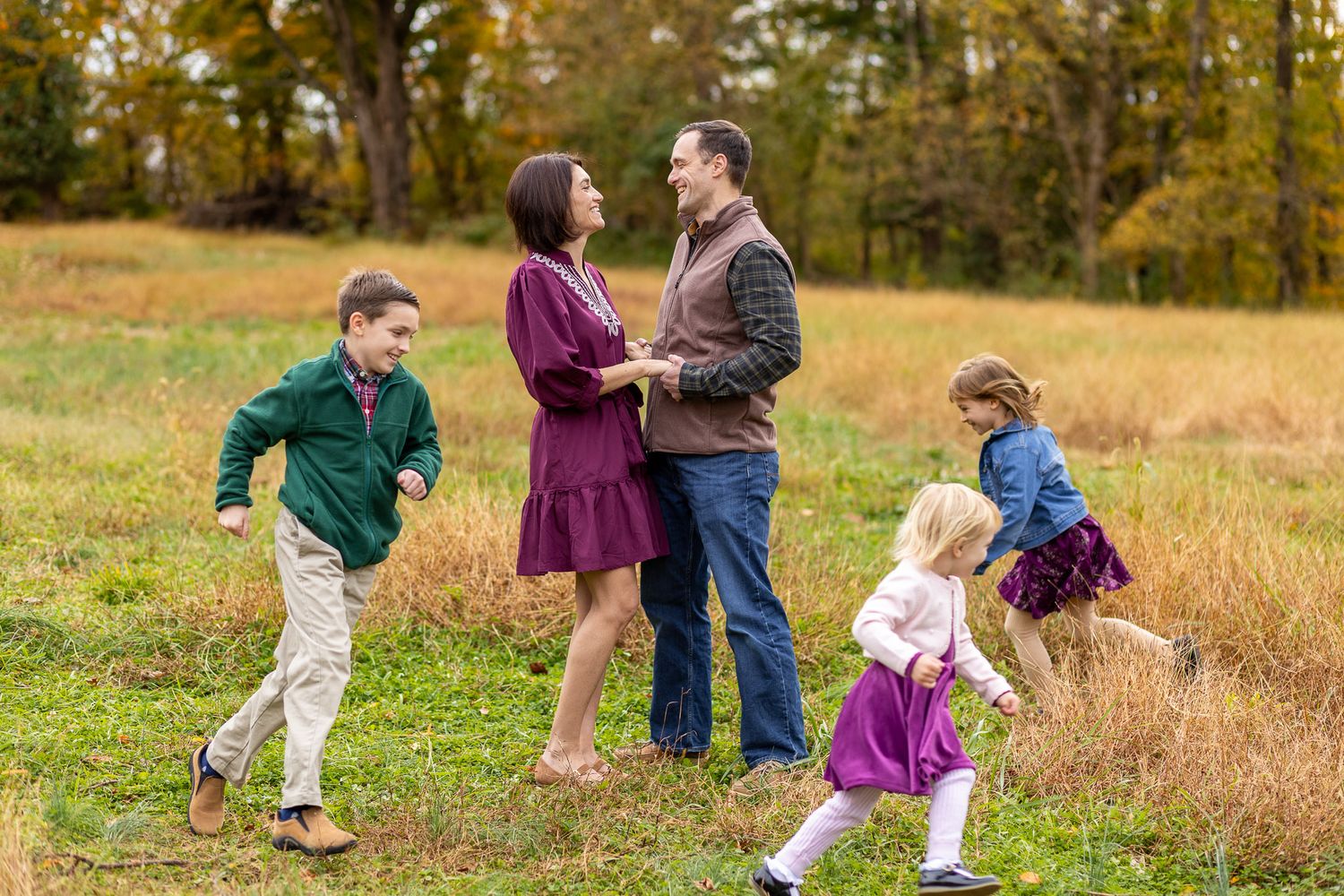 Family plays together in a golden autumn field during a lifestyle photography session at sunset.