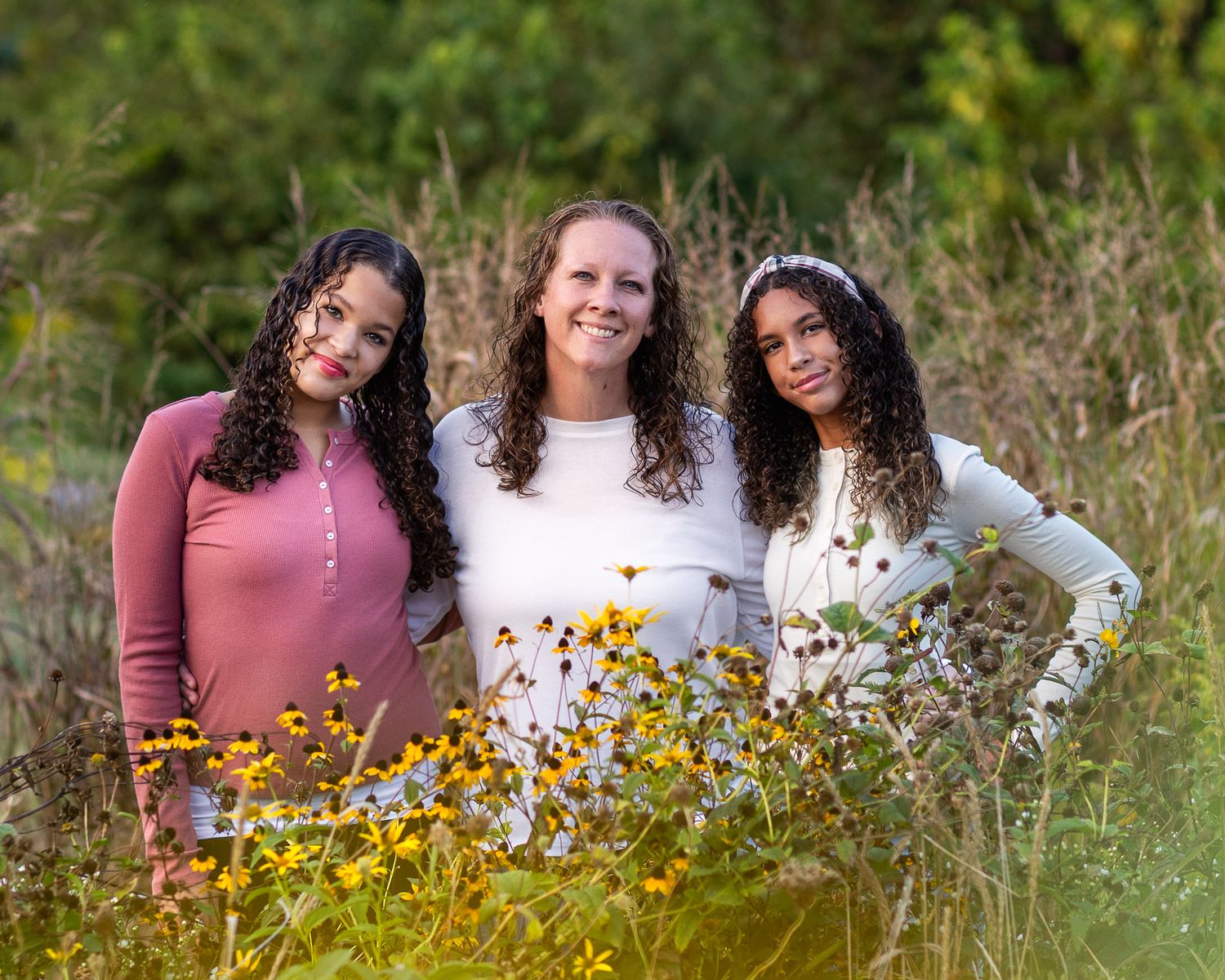 Mother and daughters together in a field of yellow wildflowers on a sunny autumn day.