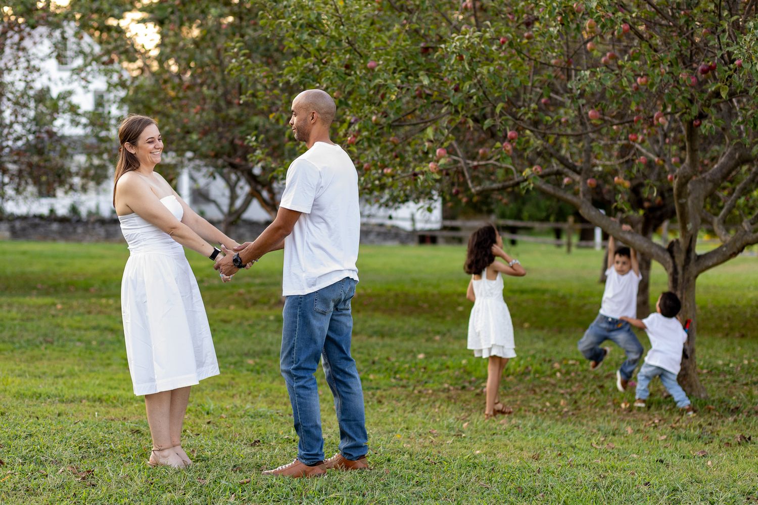 A family enjoys a sunny day together in a park setting with green trees and grass in the background.