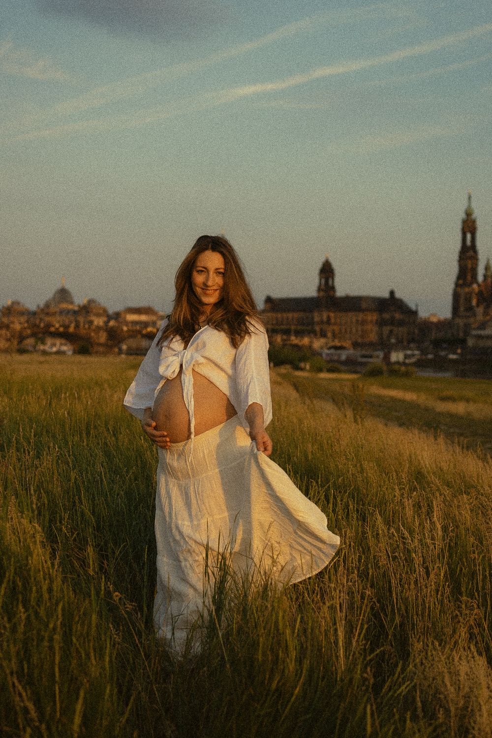 Vintage Portrait Fotoshooting mit Canalettoblick in Dresden - Schwangere Frau mit nackten Bauch, weißem Rock und Top an den Elbwiesen