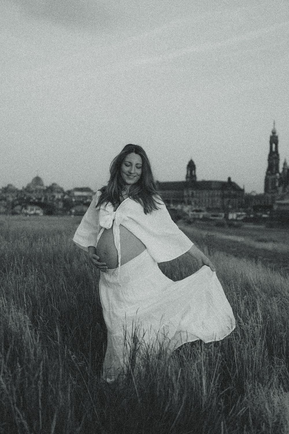 Nostalgisches Schwarz Weiß Portrait einer schwangeren Frau, die nackten Bauch anfässt und glücklich ist - Fotoshooting Elbwiesen Dresden