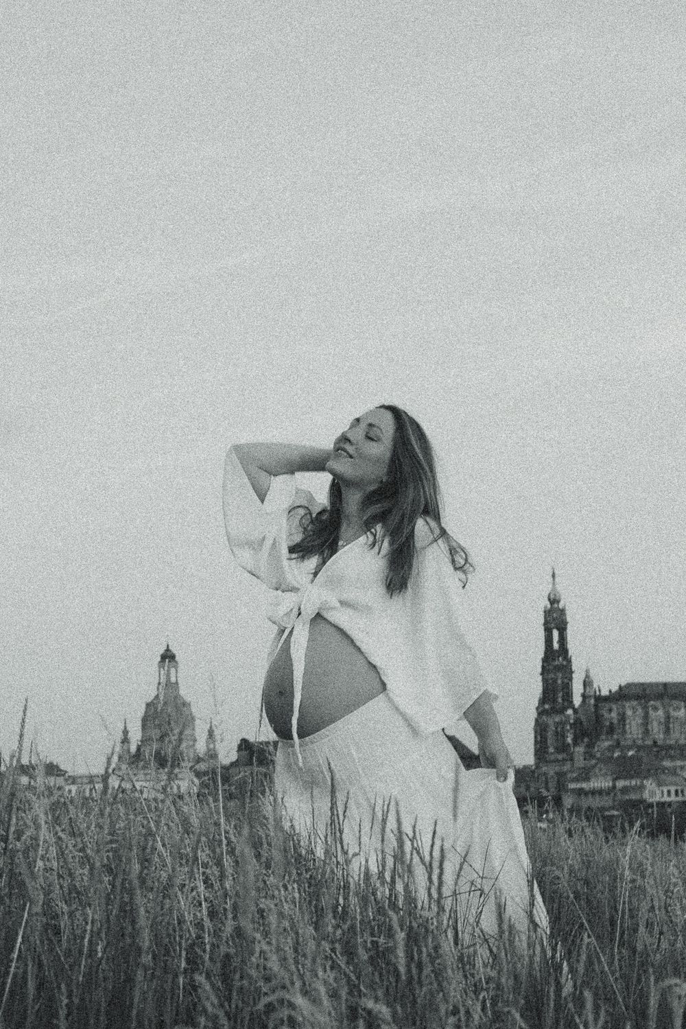 Nostalgisches Babybauchfotoshooting mit Canalettoblick in Dresden - Schwangere Frau zeigt nackten Bauch und fässt sich mit Hand durch Haare