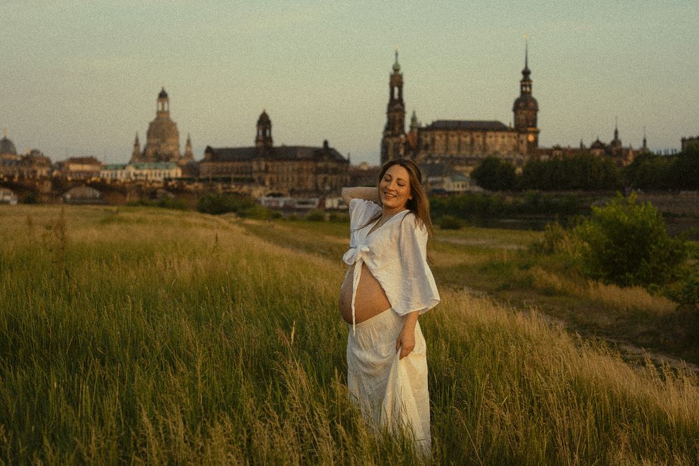 Portrait Fotoshooting einer schwangeren Bauch zur Goldenen Stunde, die über Elbwiesen geht und sich durch die Haare fässt - Altstadt Dresden