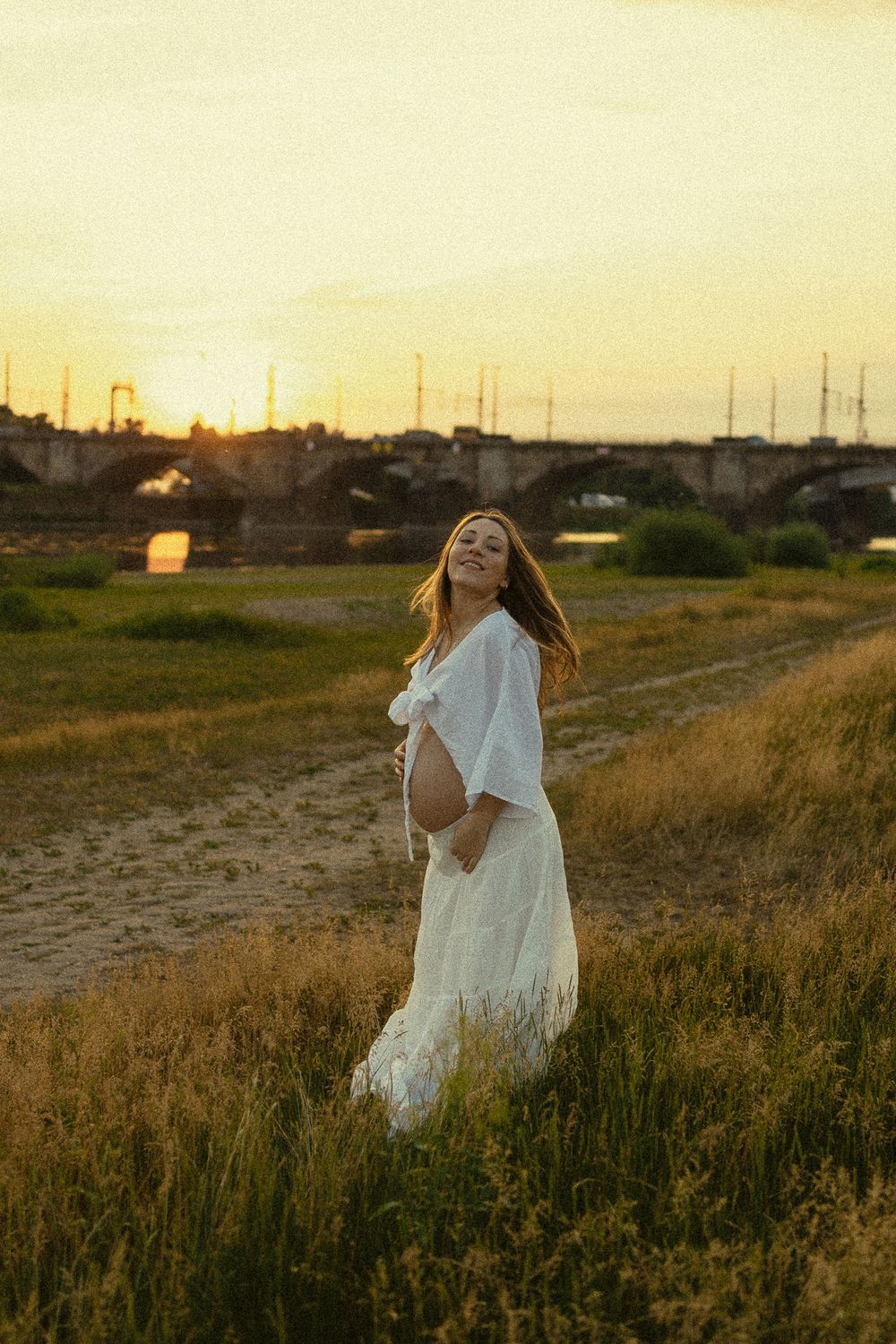 Sonnenuntergangsstimmung an den Elbwiesen in Dresden - Portrait Fotoshooting einer schwangeren Frau in Bewegung im sanften Abendlicht