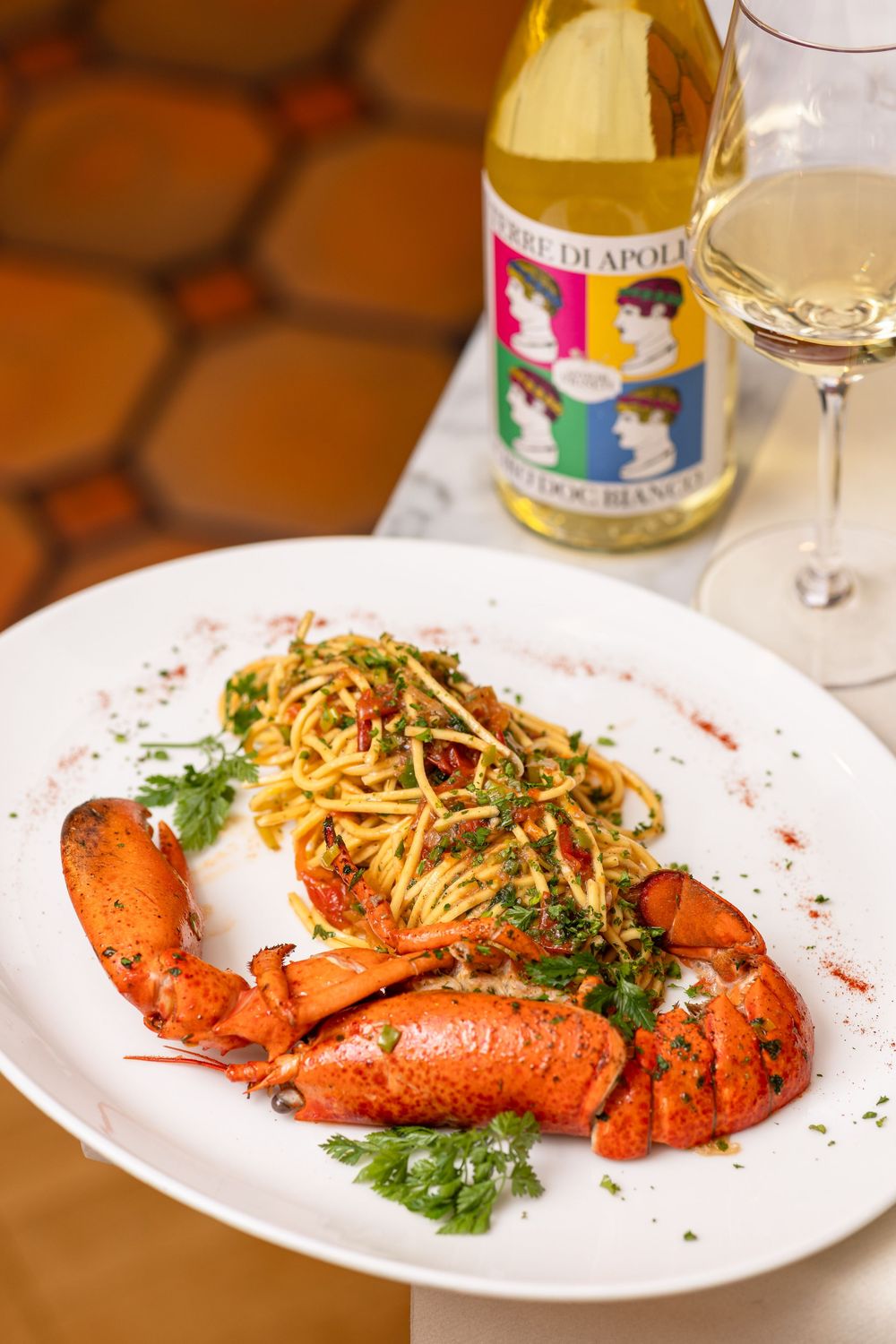 A series of plated seafood dishes featuring bright red lobster garnished with fresh herbs and served with white wine.