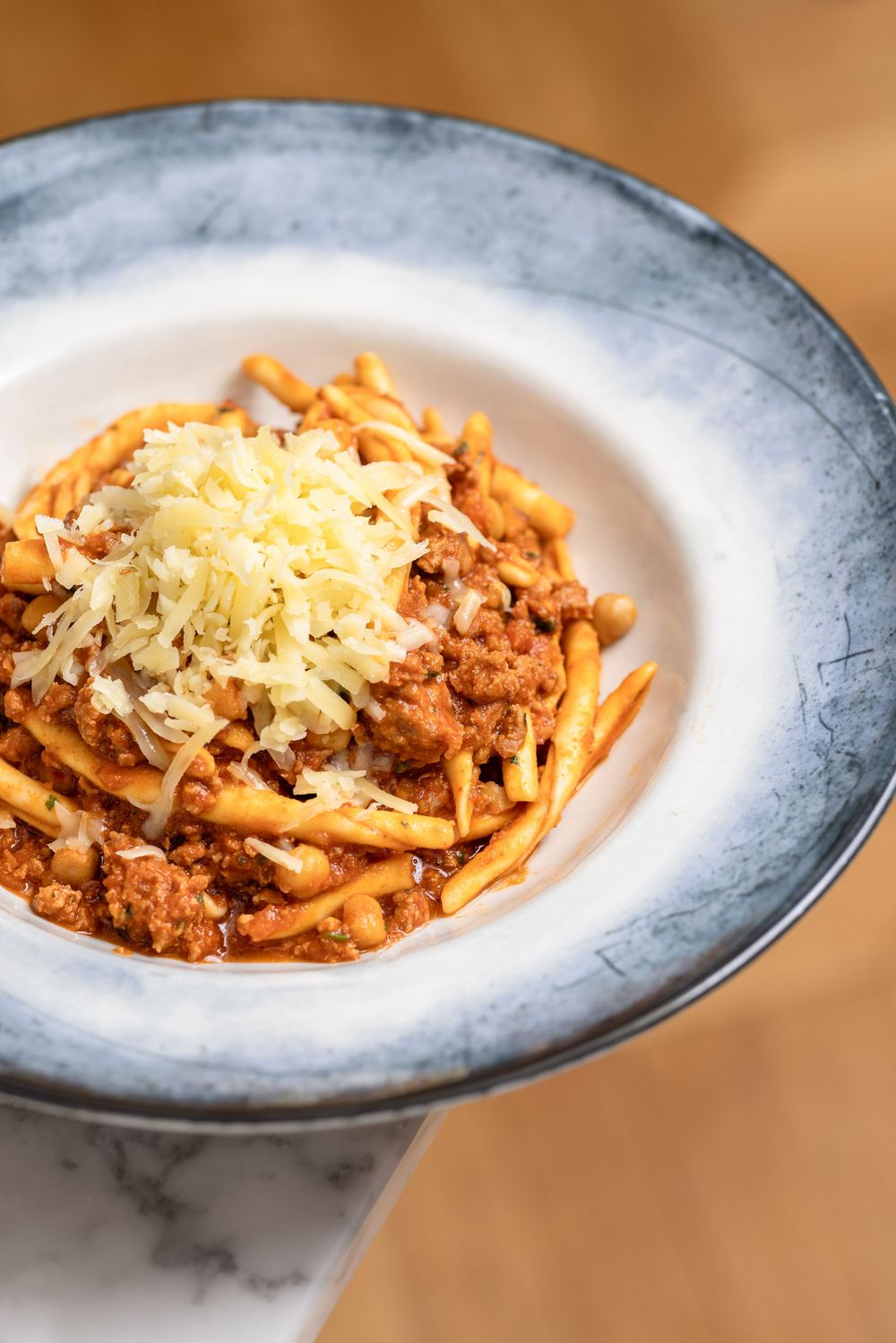 A sequence of pasta dishes topped with meat sauce and grated cheese shown at different angles on blue-rimmed plates.