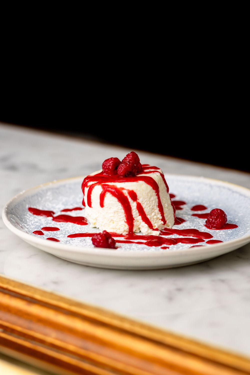 White dessert plate with raspberry sauce drizzle and fresh berries on a wooden surface.