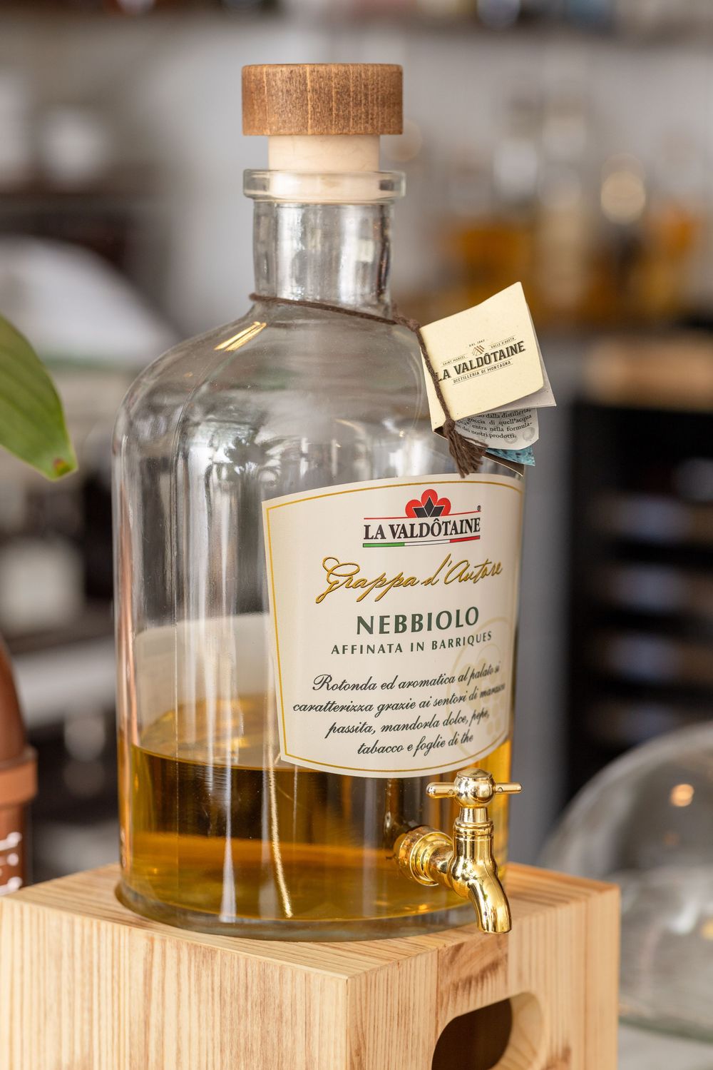 Glass bottles of Nebbiolo and Grappa Chara liquors displayed on wooden stands in a bar setting.