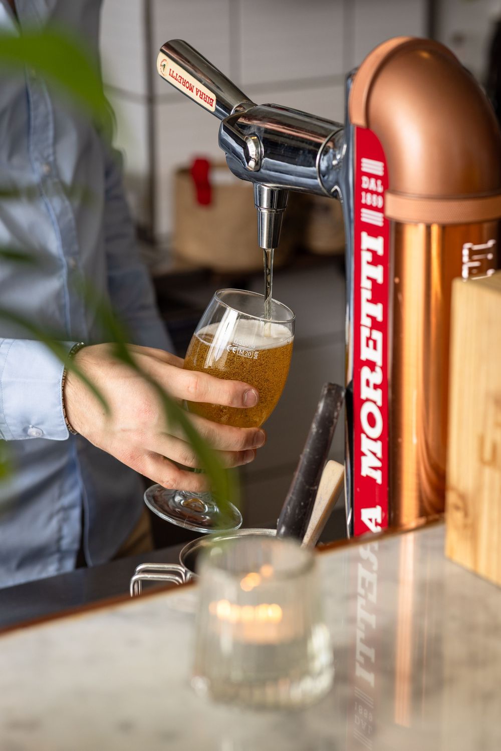 Beer being poured from tap into glass with foam forming at top in dimly lit bar setting.