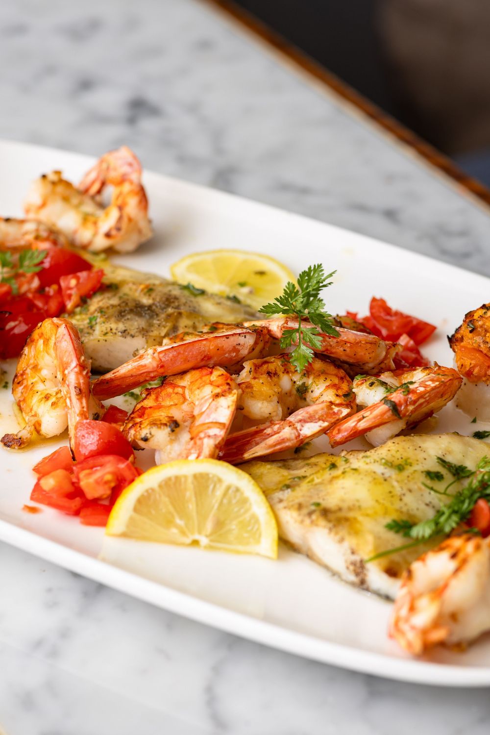 Fresh grilled shrimp with lemon and herbs arranged on a long white platter with colorful garnishes.