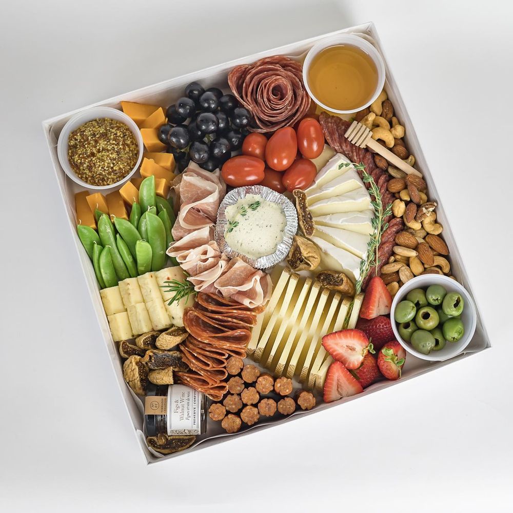 Elegant charcuterie board with meats, cheeses, fruits, nuts, olives and honey arranged in an artful display pattern.