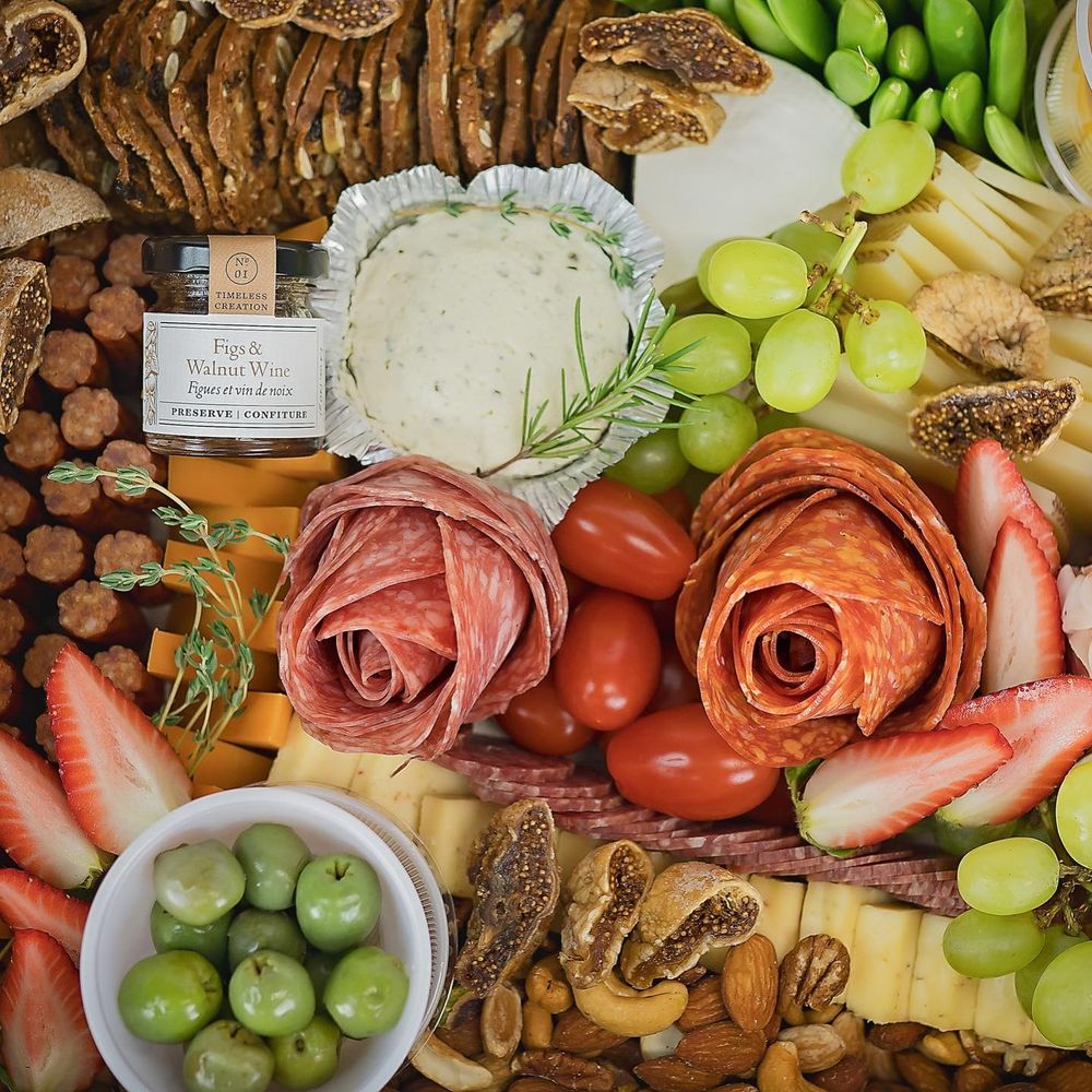 A charcuterie board with grapes, meats, cheeses, and pink roses arranged beautifully on a rustic wooden surface.