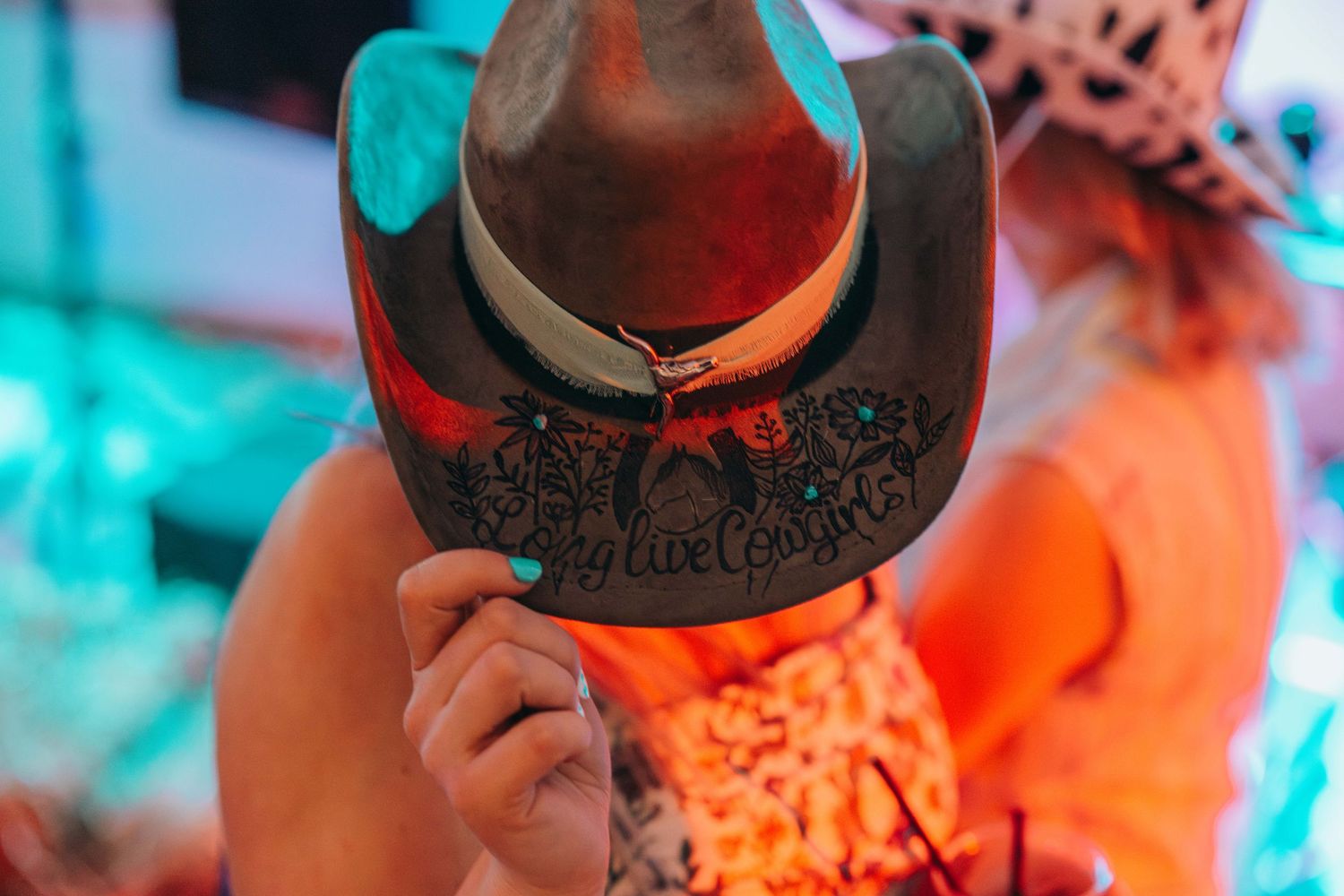 A brown cowboy hat illuminated by colorful neon lights in a party setting.