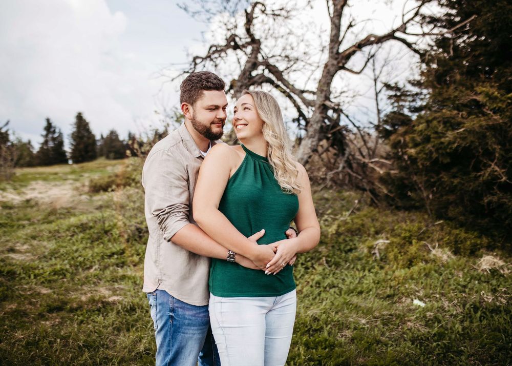 A couple embraces on a scenic mountain hillside during a romantic outdoor photo session.