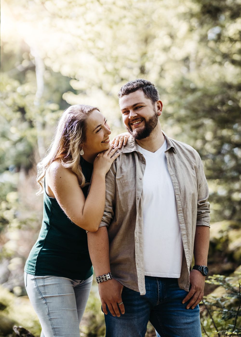 A couple shares joyful moments together in a sunlit forest setting wearing casual outfits.