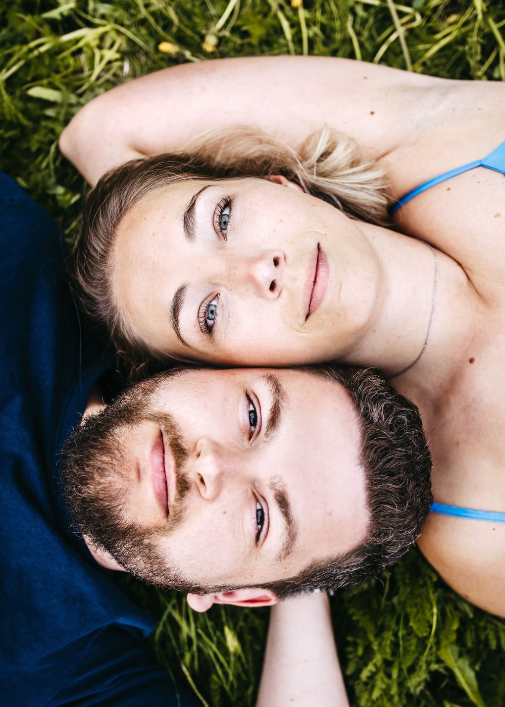 A couple lying on green grass together on a sunny day, shot from above in an intimate portrait style.
