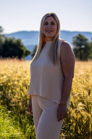 A person in a cream-colored dress poses in a golden wheat field at sunset with mountains in the background.