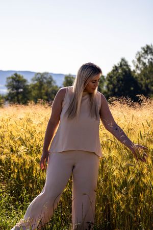 A person in beige outfit stands in a golden wheat field at sunset with mountains and trees in the background.