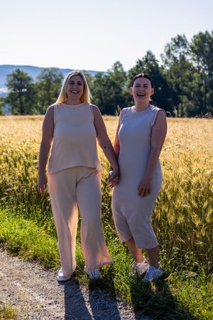 Two people wearing matching beige outfits pose together in a sunny wheat field on a summer day.