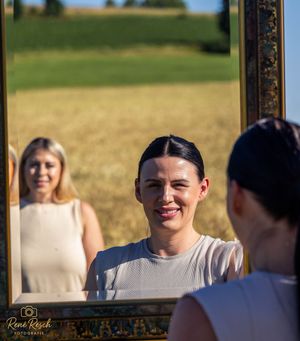 Wedding party members smile and laugh together while standing outdoors in front of a golden wheat field.