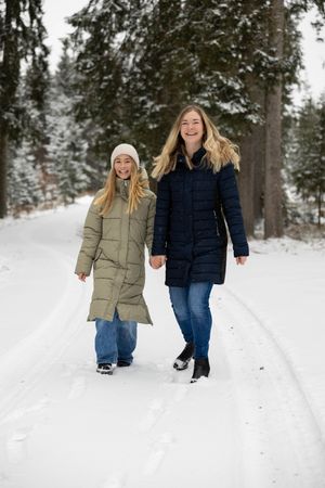 Two people walk hand in hand through a snowy forest path wearing winter coats and jeans on a cold winter day.