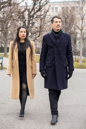 Two people walking outdoors wearing winter coats, one in camel and one in navy, photographed from different angles.