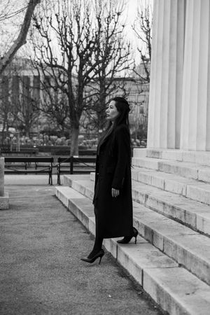 A person in black attire sits contemplatively on white marble steps against a winter landscape backdrop.