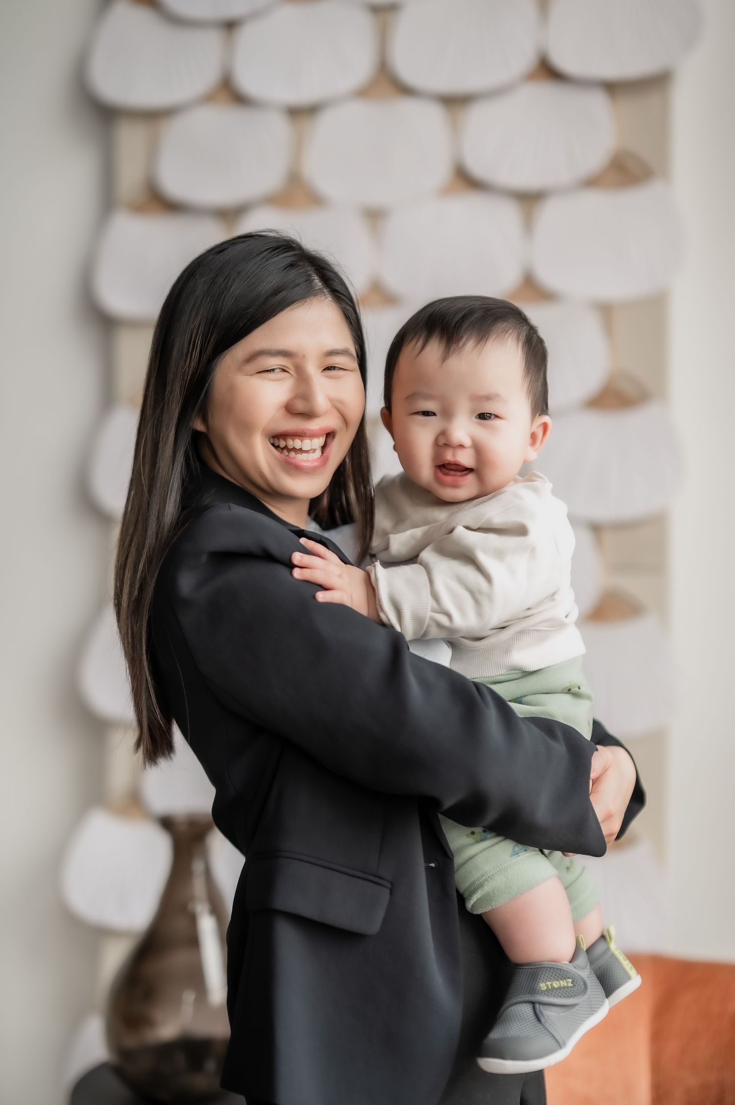 A joyful parent and baby share tender moments together against a white textured wall background.