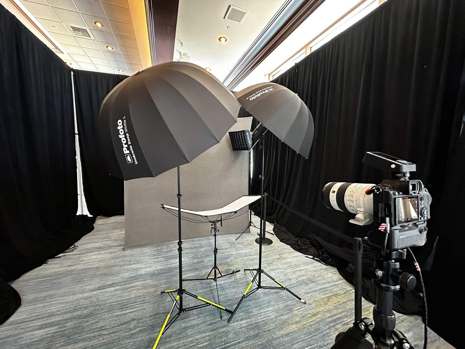 Professional photography studio setup with multiple lighting equipment and umbrellas against black backdrop.