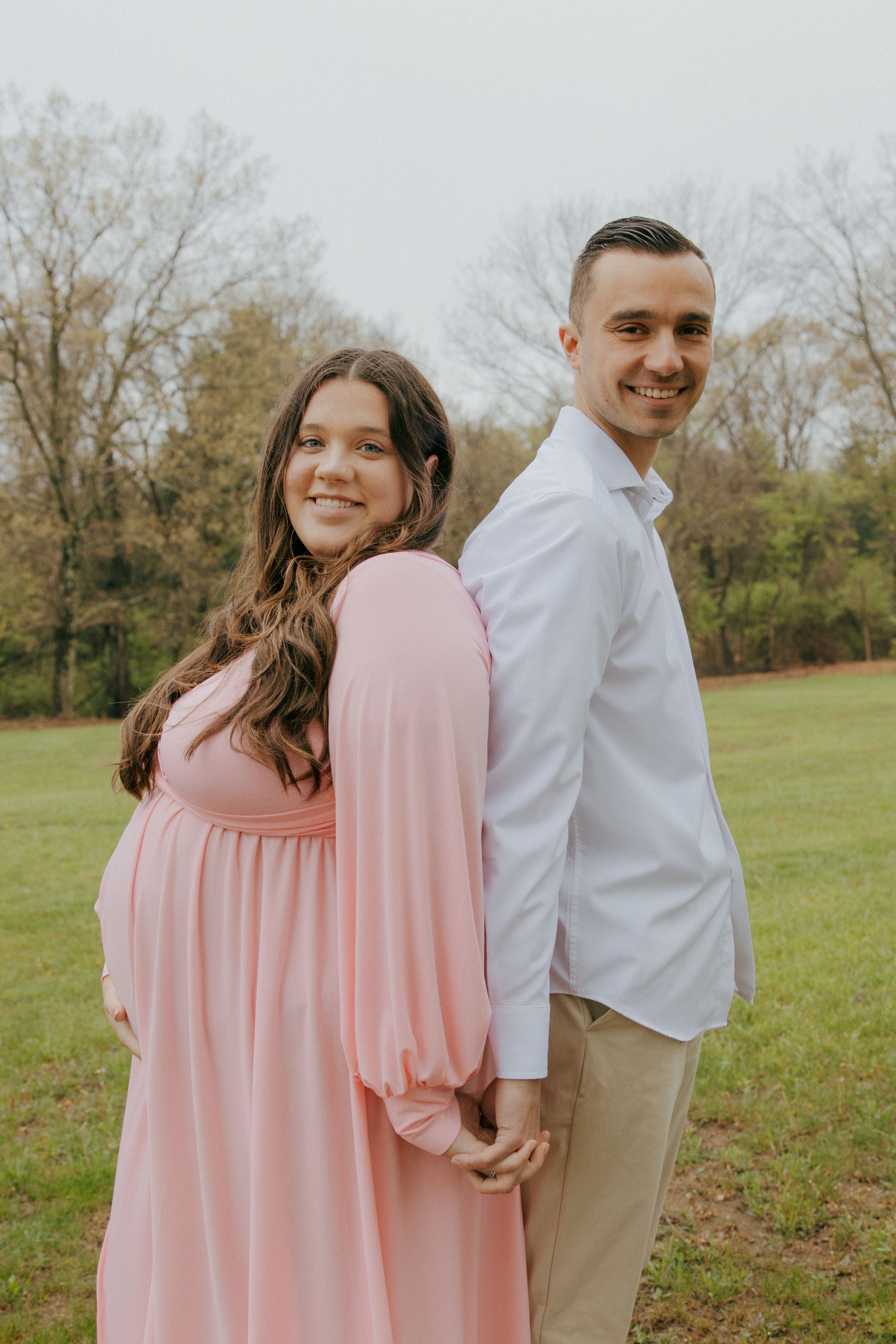 A couple smiles while standing back-to-back in a spring outdoor setting.