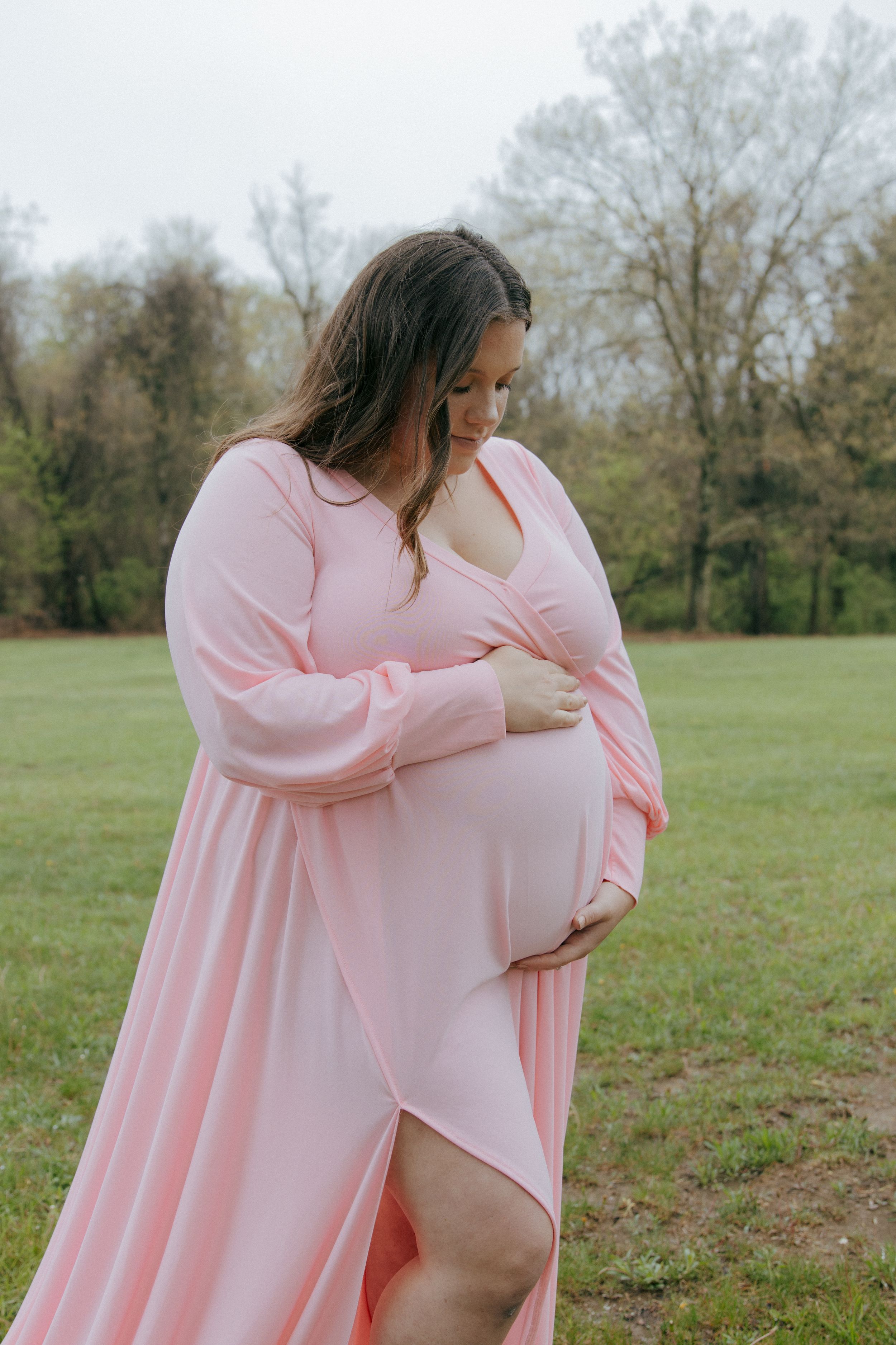 A flowing pink maternity dress catches the light in an outdoor portrait session.