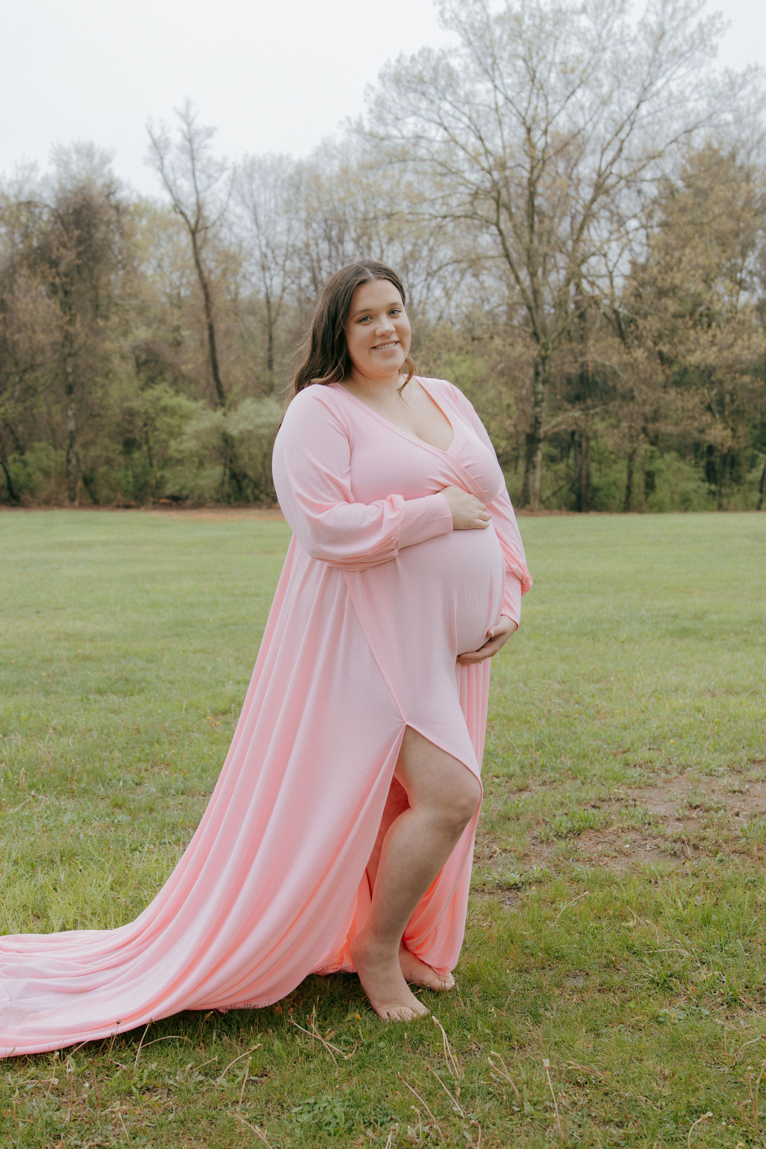 A person in a flowing pink dress poses gracefully on a grassy field during a photo shoot.
