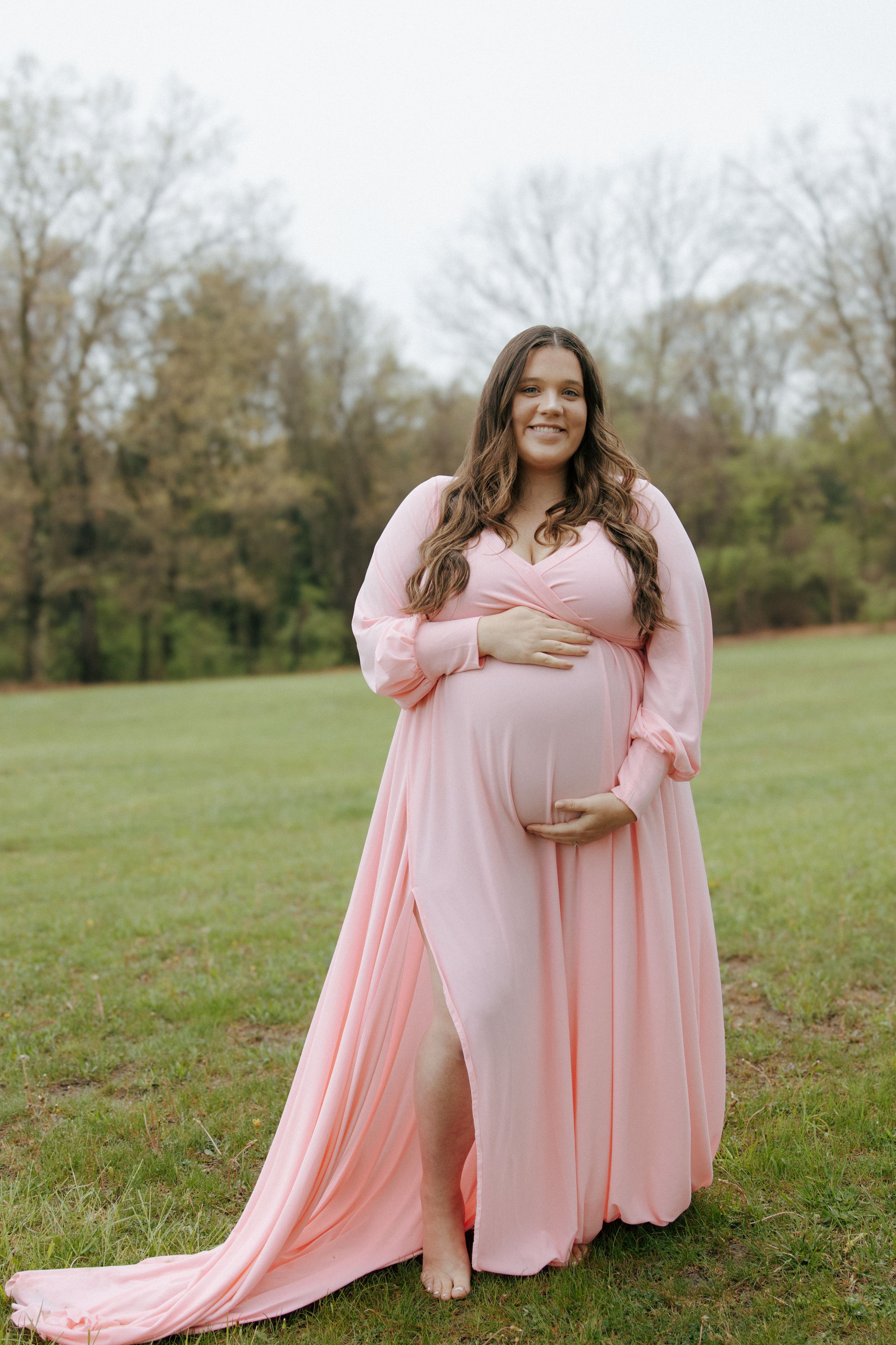 A maternity photo session features a pink dress in a serene outdoor setting.