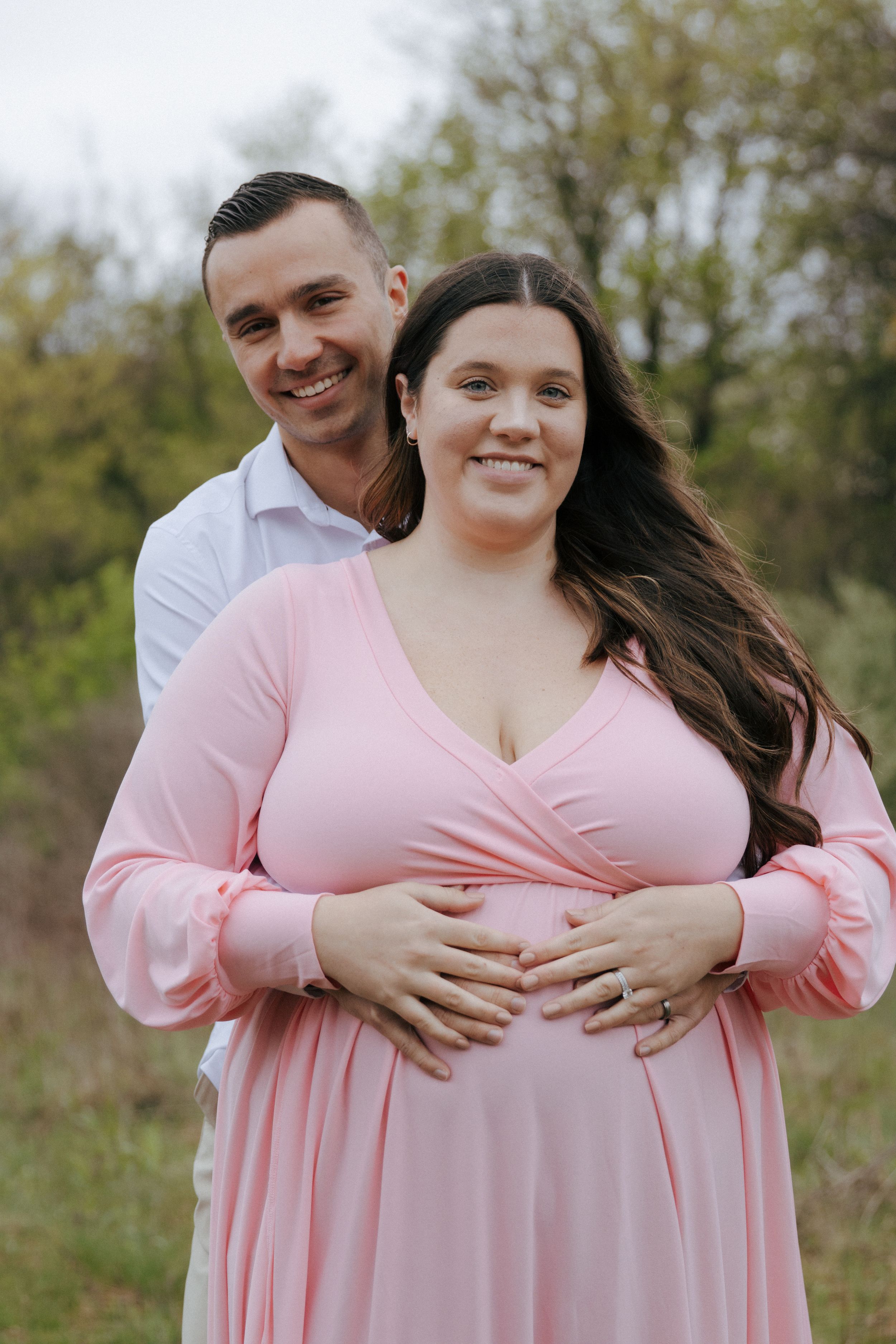 A couple shares intimate moments during their maternity photoshoot in a grassy field.