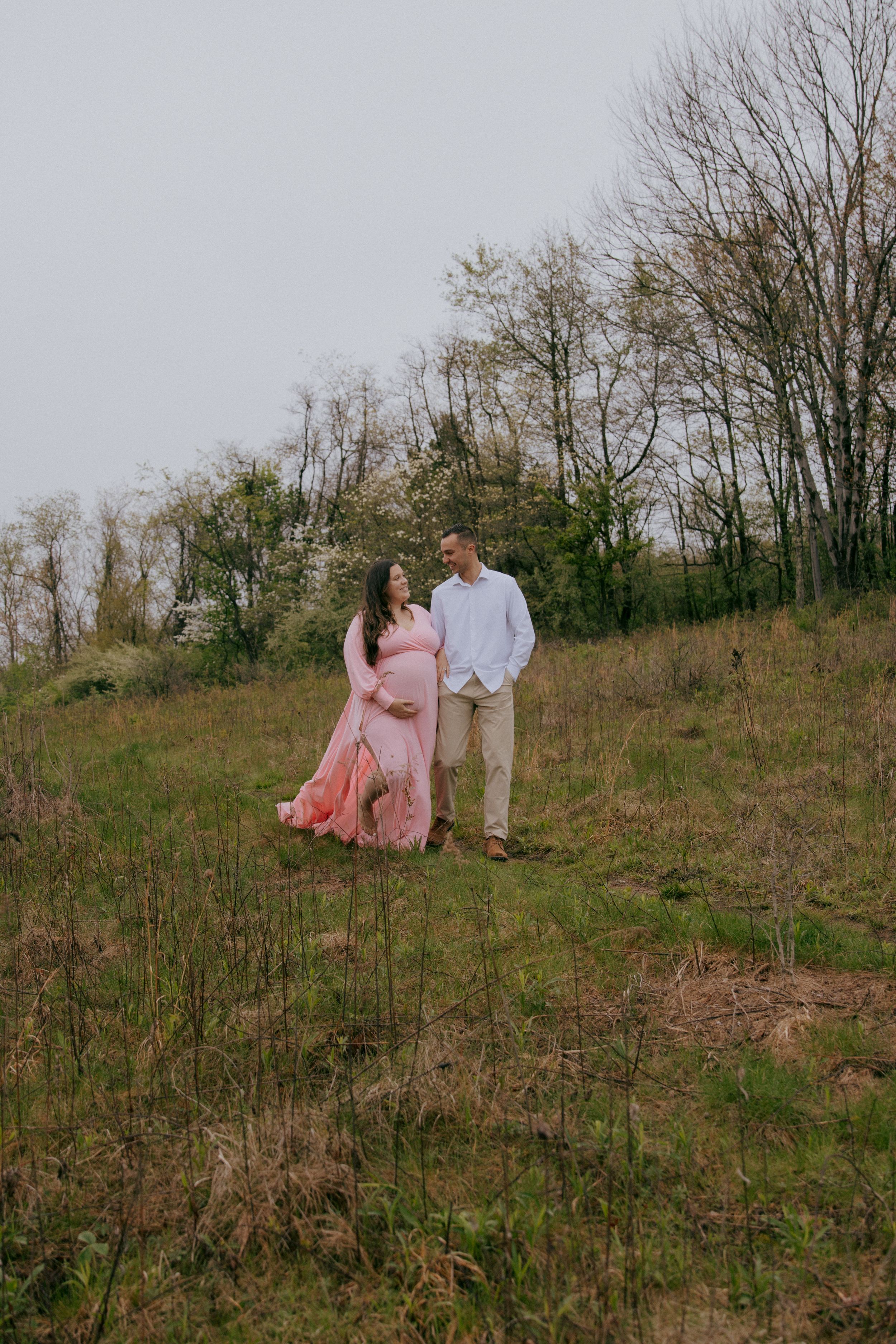 A couple shares romantic moments on a hillside during their maternity photoshoot.