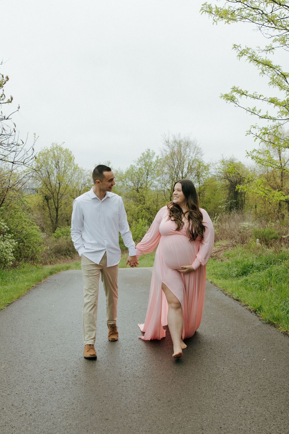A couple shares a playful moment while walking on a paved trail in nature.