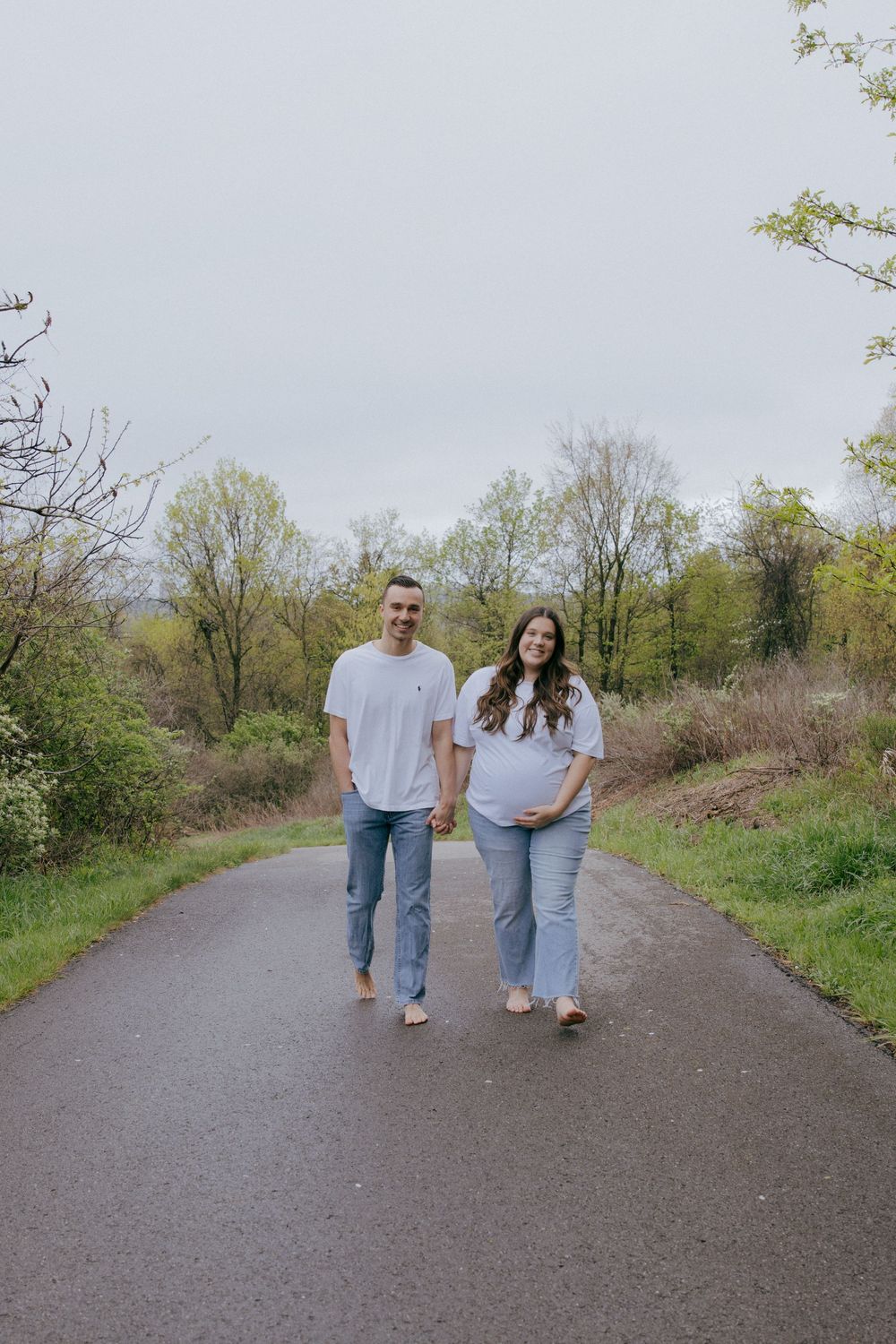 A couple in coordinated casual outfits walks hand in hand on a nature trail.