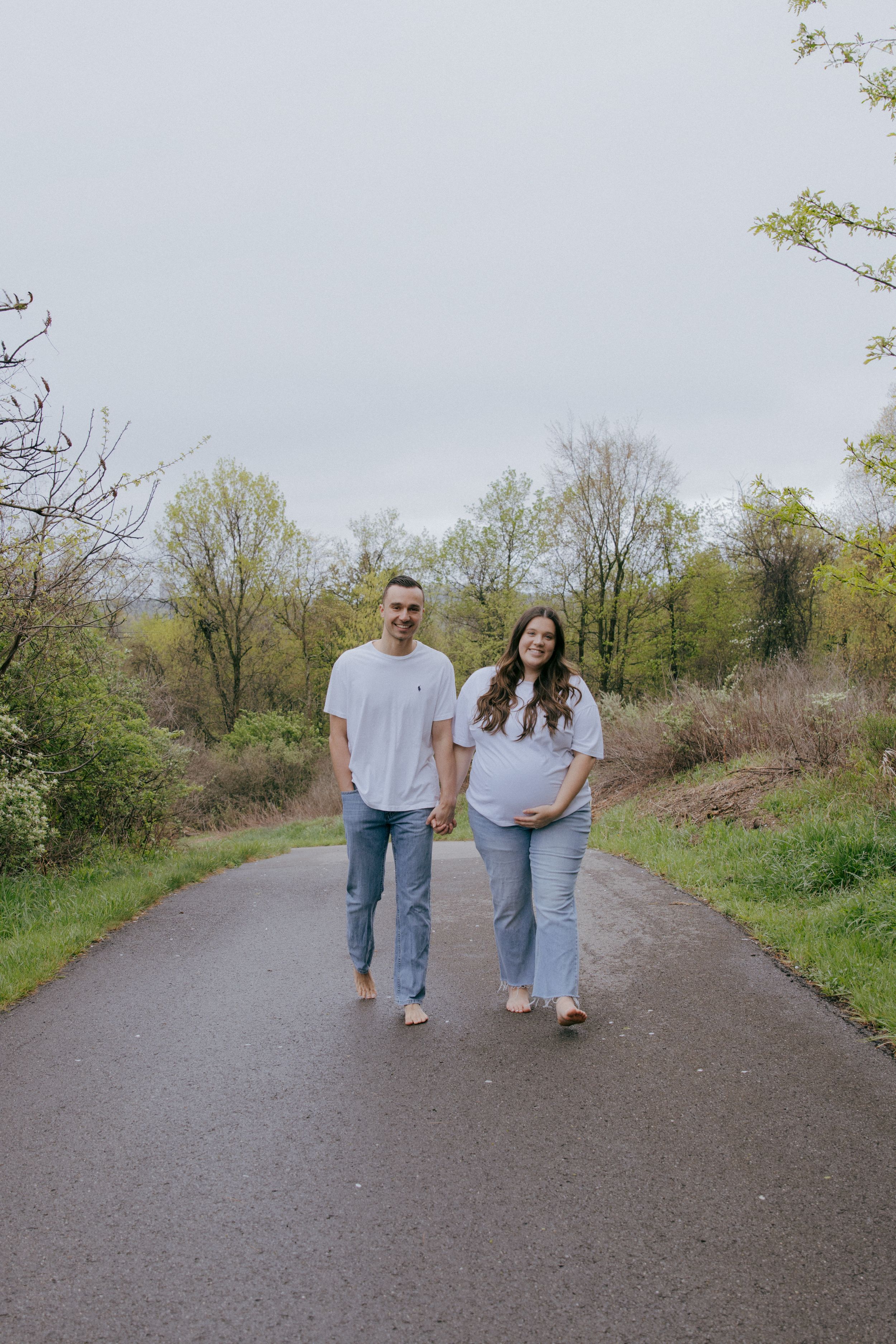 A couple in coordinated casual outfits walks hand in hand on a nature trail.