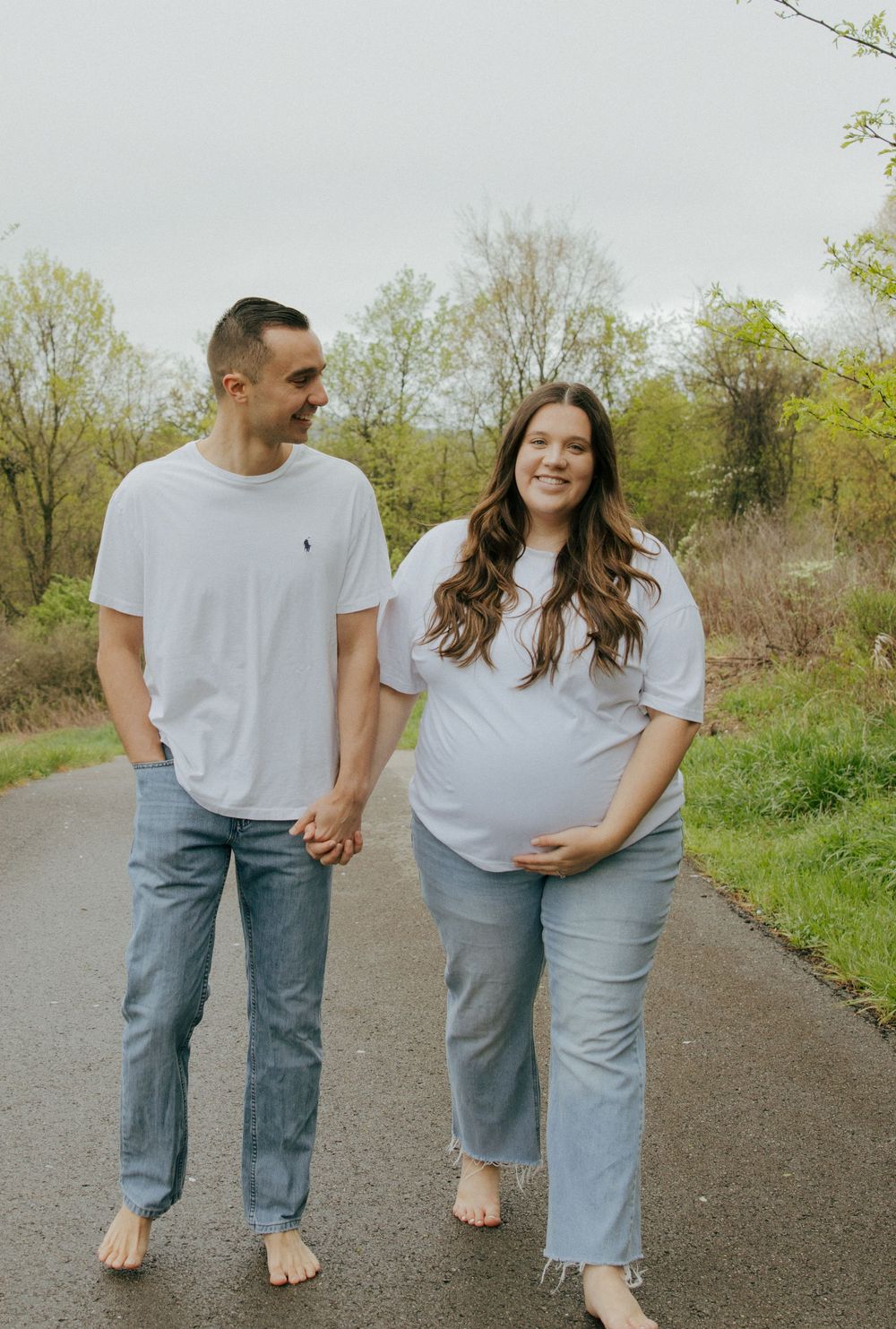 A couple walks barefoot together on a dirt path surrounded by spring greenery.