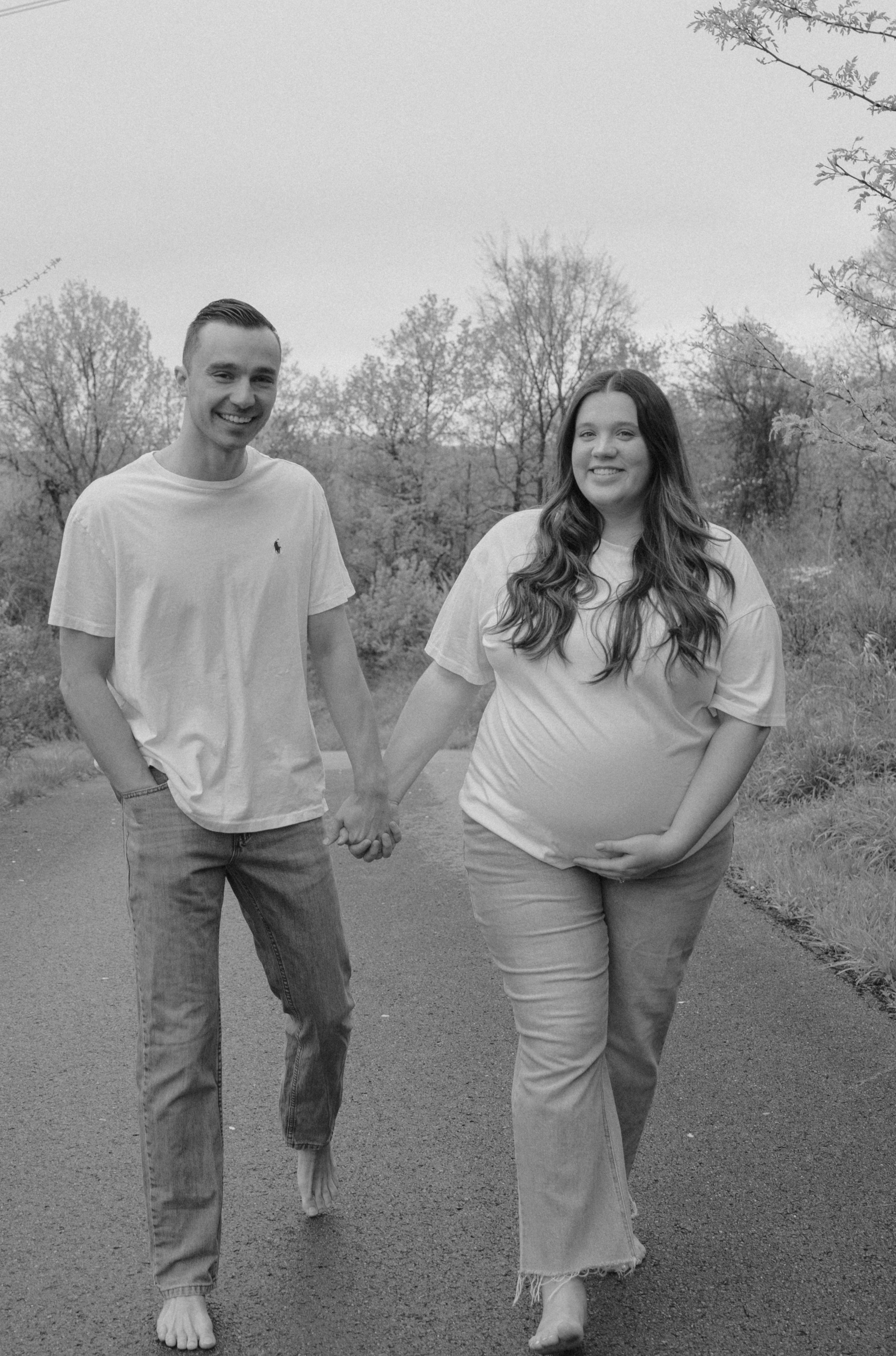 A black and white photo shows a couple sharing joyful moments on an outdoor path.