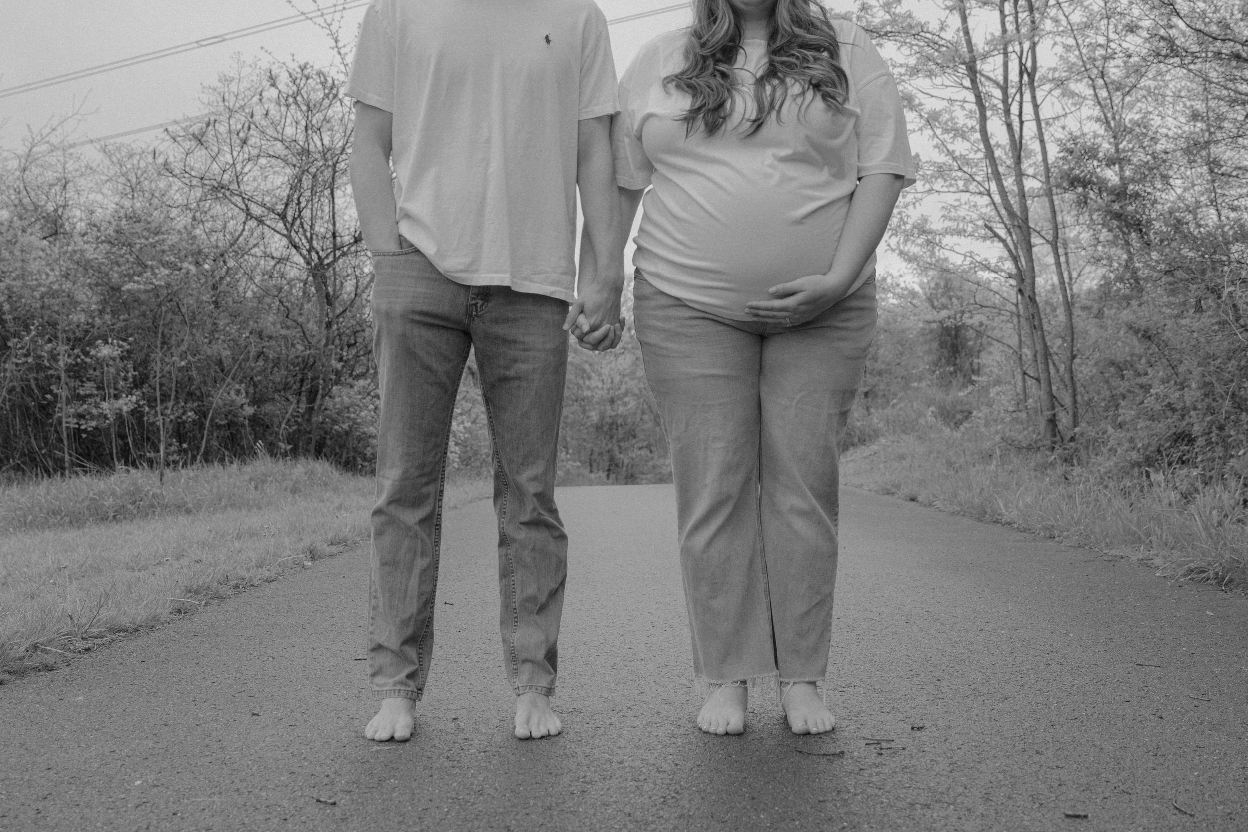 Black and white photo showing legs and feet of a couple standing on a path outdoors.