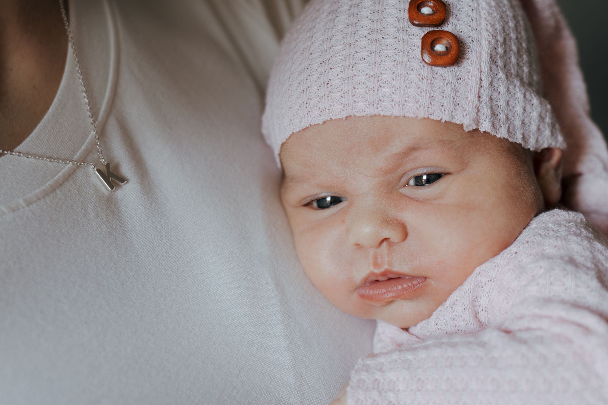 Sweet portrait of sleeping newborn wearing pink clothing and white knit hat.
